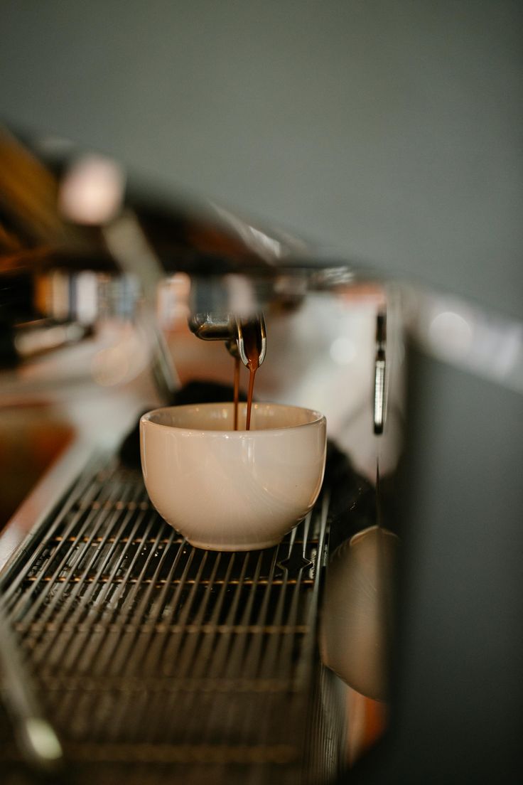 A double espresso pulling from the group head of the machine into a small pale ceramic cup, the crema falling in two thin ribbons.