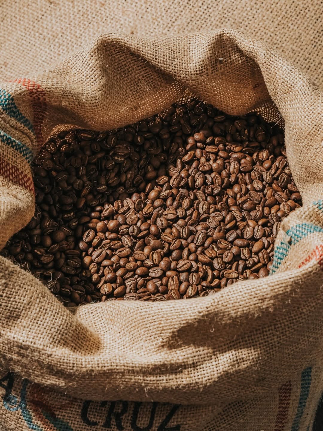An open burlap sack brimming with freshly roasted coffee beans, sunlight catching the folds of the coarse woven fabric.
